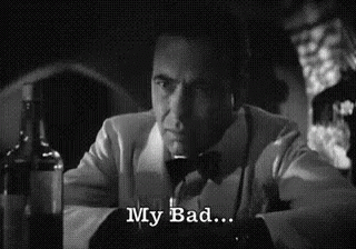 a man in a suit and bow tie is sitting at a table with a glass of wine and a bottle of alcohol .