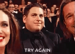 A Man In A Suit And Bow Tie Is Sitting In Front Of A Crowd Of People And Says `` Try Again '' . GIF