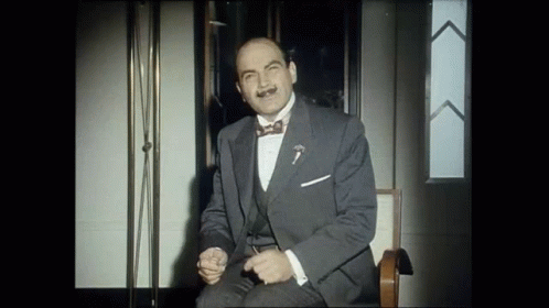 A Man In A Suit And Bow Tie Is Sitting On A Chair GIF