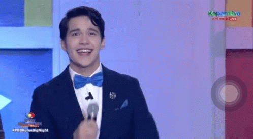 A Man In A Suit And Bow Tie Is Smiling While Standing In Front Of A Microphone . GIF