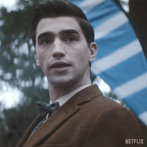 A Man In A Suit And Bow Tie Is Standing In Front Of A Blue And White Striped Flag And A Netflix Logo GIF