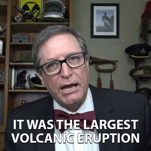 A Man In A Suit And Bow Tie Is Talking About The Largest Volcanic Eruption GIF