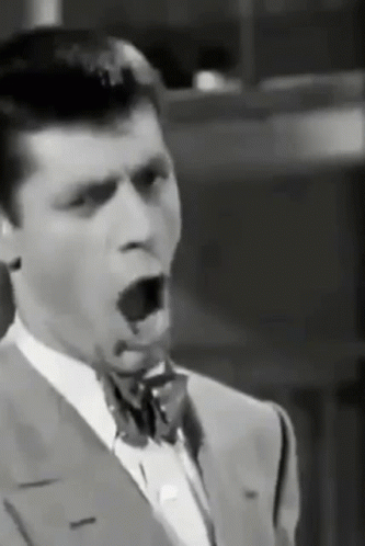 A Man In A Suit And Bow Tie Is Yawning . GIF