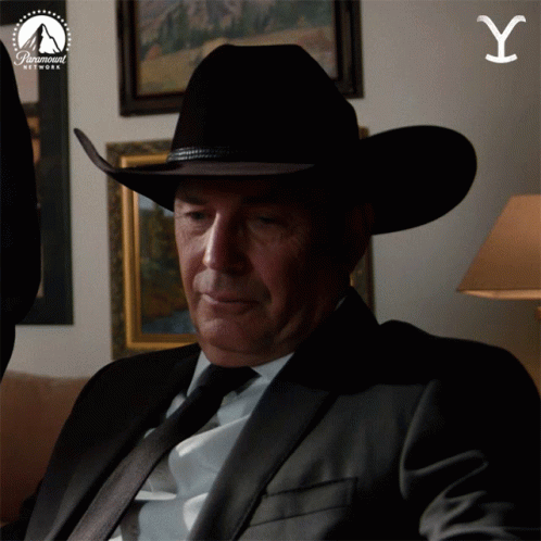 A Man In A Suit And Cowboy Hat Is Sitting In Front Of A Paramount Network Sign GIF