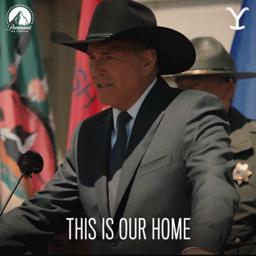 A Man In A Suit And Cowboy Hat Stands At A Podium With The Words " This Is Our Home " Below Him GIF