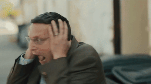 A Man In A Suit And Glasses Is Holding His Head GIF