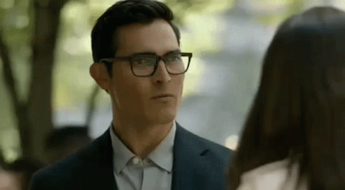 A Man In A Suit And Glasses Is Looking At A Woman In A White Shirt . GIF
