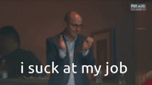A Man In A Suit And Glasses Is Looking At His Phone With The Words I Suck At My Job Behind Him GIF