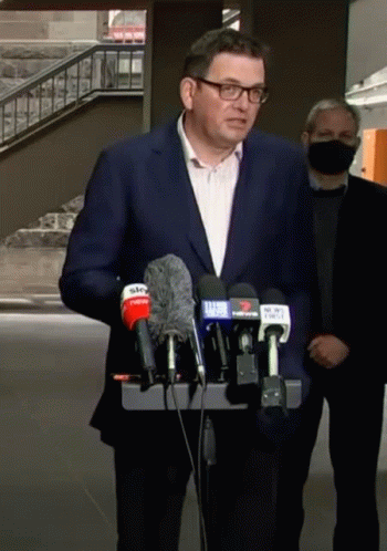 A Man In A Suit And Glasses Is Standing In Front Of A Podium With Microphones . GIF