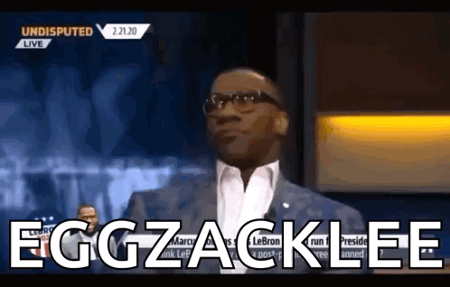 A Man In A Suit And Glasses Says Eggzacklee On A Television Show . GIF