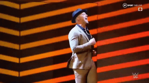A Man In A Suit And Hat Is Dancing On A Stage In Front Of A Striped Background . GIF