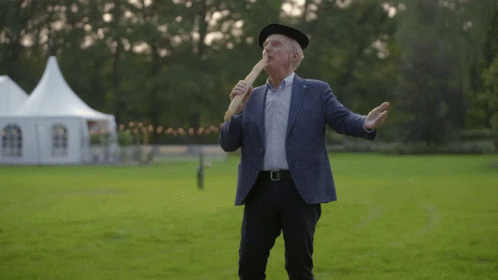 A Man In A Suit And Hat Is Holding A Bread Stick In His Mouth GIF