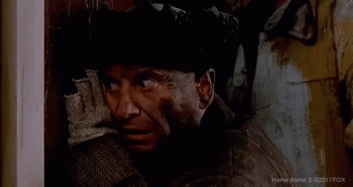 A Man In A Suit And Hat Is Looking Out A Doorway . GIF