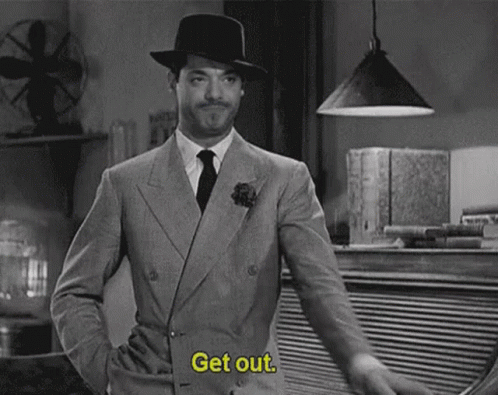A Man In A Suit And Hat Is Standing In A Room And Says `` Get Out '' . GIF