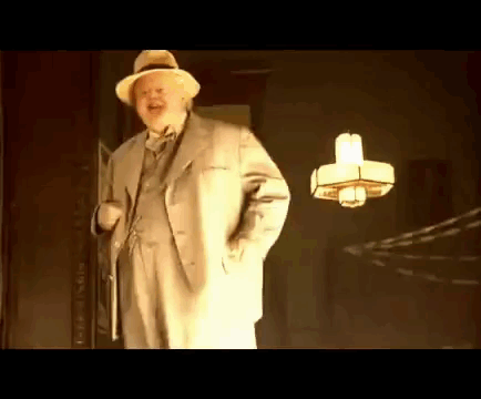 A Man In A Suit And Hat Is Standing In Front Of A Lamp . GIF