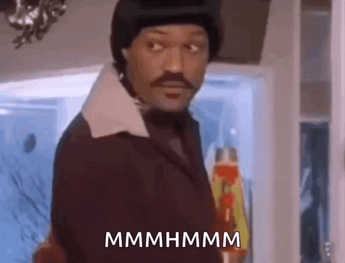 A Man In A Suit And Hat Is Standing In Front Of A Refrigerator And Holding A Bottle Of Ketchup . GIF