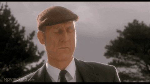 A Man In A Suit And Hat Is Standing In Front Of Some Trees . GIF