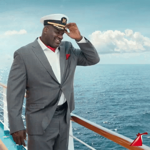 A Man In A Suit And Hat Is Standing On A Cruise Ship GIF