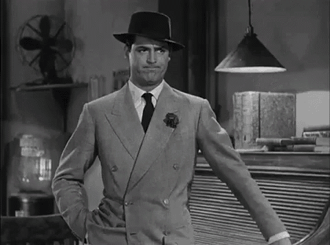 A Man In A Suit And Hat Is Standing With His Hands In His Pockets In A Black And White Photo . GIF