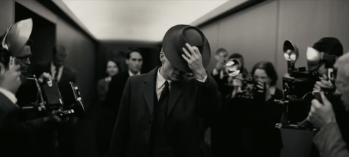 A Man In A Suit And Hat Is Surrounded By People Taking Pictures GIF