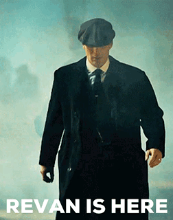 A Man In A Suit And Hat Is Walking In Front Of A Sign That Says ' Revan Is Here ' . GIF