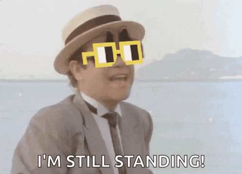 A Man In A Suit And Hat Is Wearing Sunglasses And Says I 'M Still Standing GIF