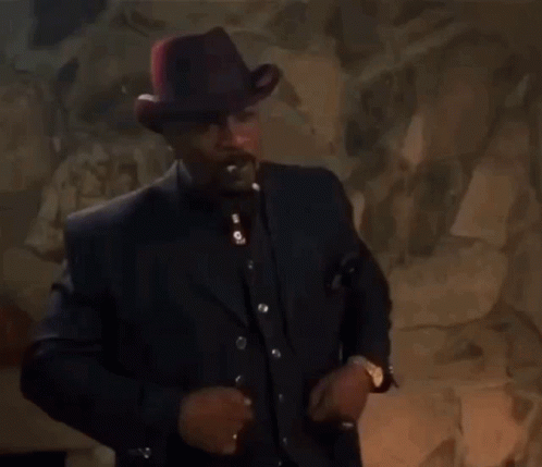 A Man In A Suit And Hat Smoking A Cigarette GIF