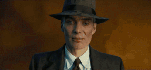 A Man In A Suit And Hat Stands In Front Of A Fire GIF