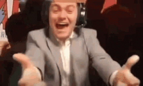 A Man In A Suit And Headphones Is Laughing With His Arms Outstretched In Front Of A Crowd . GIF