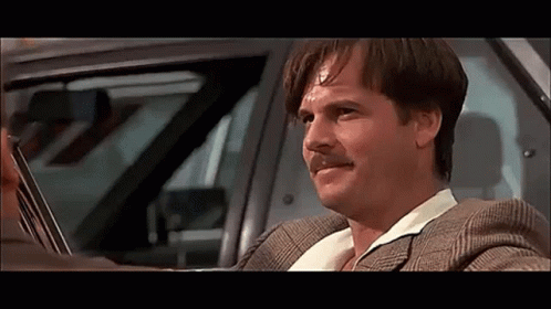 A Man In A Suit And Mustache Is Driving A Car . GIF
