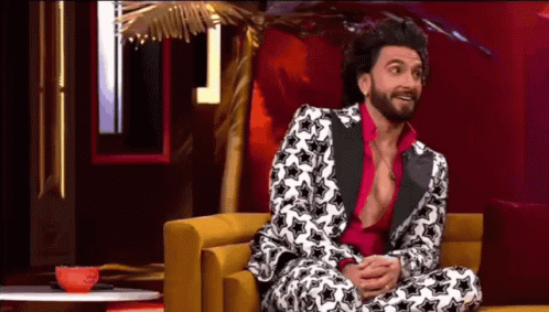 A Man In A Suit And Pink Shirt Is Sitting On A Couch . GIF