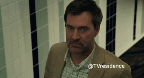 A Man In A Suit And Plaid Shirt Is Standing In A Hallway With The Hashtag @Tvresidence GIF