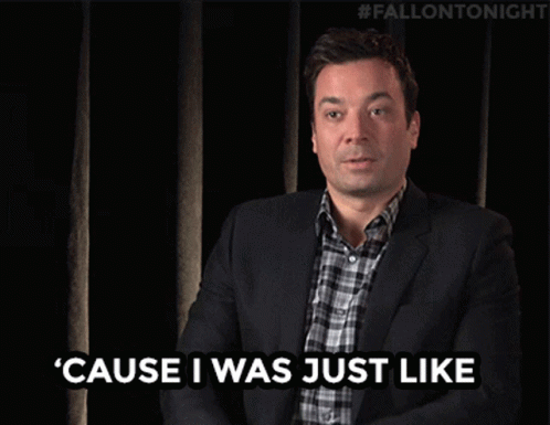 A Man In A Suit And Plaid Shirt Is Waving His Hand In Front Of A Black Curtain With #Fallontonight Written On It GIF