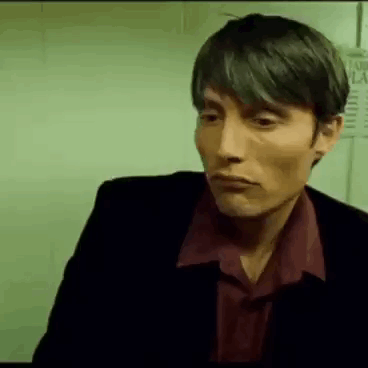 A Man In A Suit And Red Shirt Is Looking At The Camera . GIF