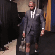 A Man In A Suit And Shorts Holds A Bag GIF