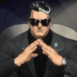 a man in a suit and sunglasses is sitting in a chair with his hands folded in front of him .