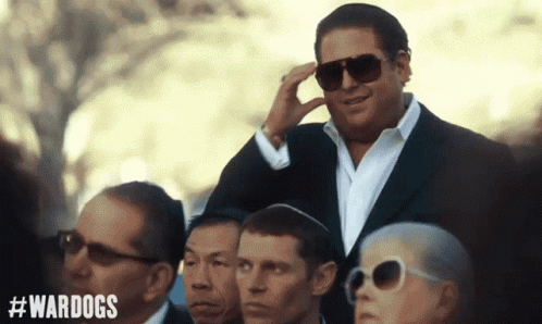 A Man In A Suit And Sunglasses Stands In A Crowd With #Wardogs On The Bottom GIF