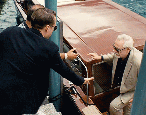 A Man In A Suit And Sunglasses Talks To Another Man In A Boat GIF