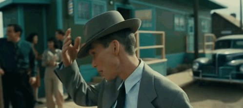 A Man In A Suit And Tie Adjusts His Hat In Front Of A Barber Shop GIF