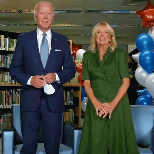A Man In A Suit And Tie And A Woman In A Green Dress Stand Next To Each Other GIF