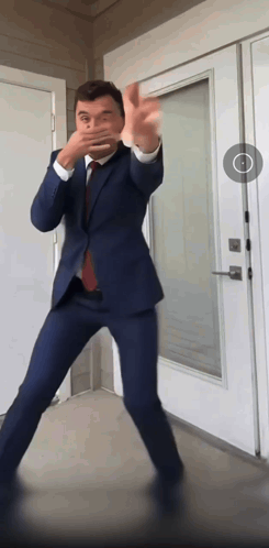 A Man In A Suit And Tie Dancing In Front Of A White Door GIF