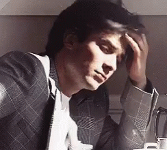 A Man In A Suit And Tie Has His Hand On His Forehead GIF