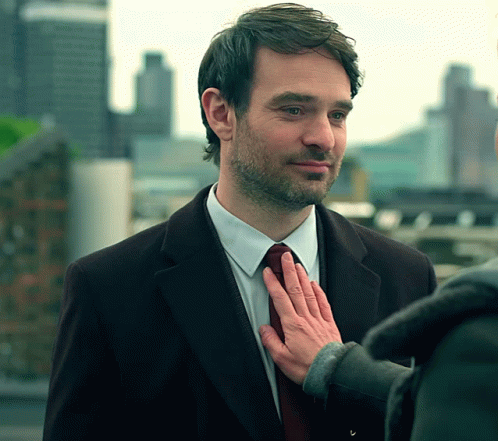 A Man In A Suit And Tie Has His Hand On His Tie GIF