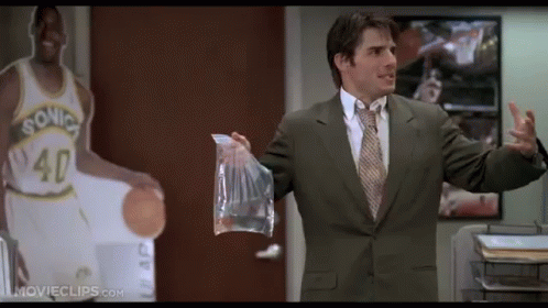 A Man In A Suit And Tie Holds A Bag In Front Of A Sonics Basketball Player GIF