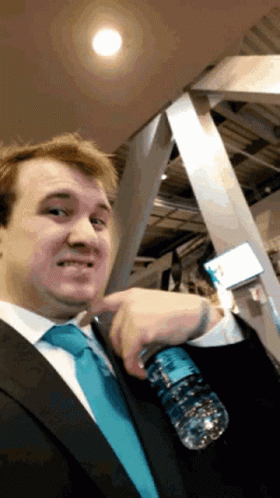 A Man In A Suit And Tie Holds A Bottle Of Water GIF