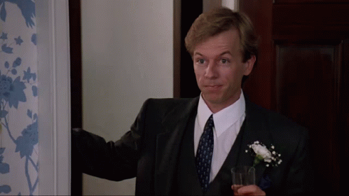 A Man In A Suit And Tie Holds A Glass In His Hand GIF