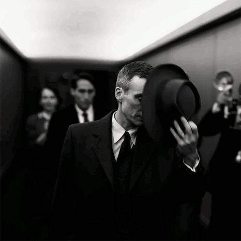A Man In A Suit And Tie Holds A Hat Over His Face GIF