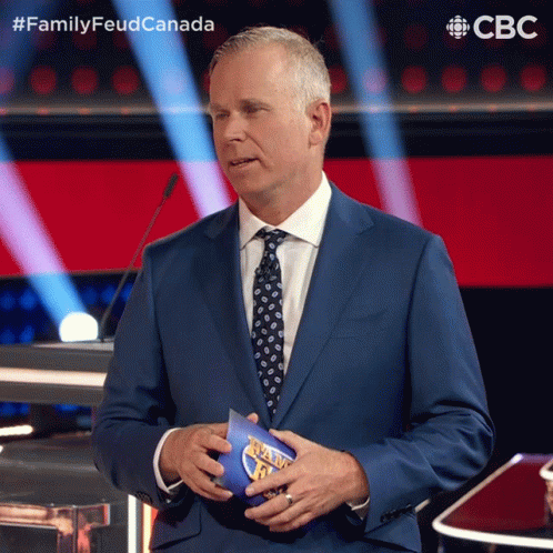 A Man In A Suit And Tie Holds A Piece Of Paper That Says Family Feud Canada On It GIF