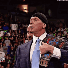A Man In A Suit And Tie Holds A Wrestling Belt Over His Shoulder GIF