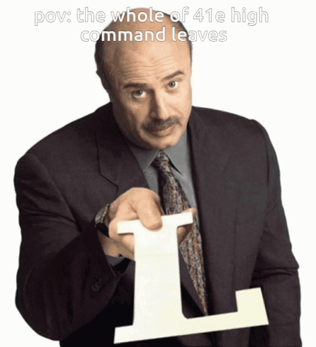 A Man In A Suit And Tie Holds Up A Large L GIF
